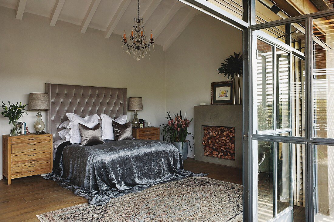 Grossräumiges Schlafzimmer unter dem Dach, silberfarbenes, glänzendes Plaid auf Doppelbett, mit hohem Polster Kopfteil an Wand