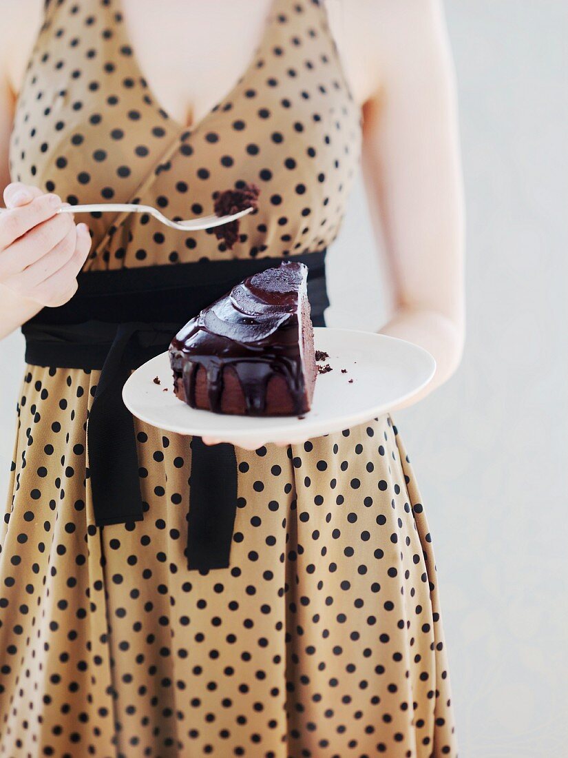 A woman in a spotted dress eating a slice of chocolate cake