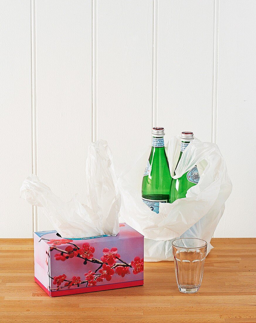 Empty tissue box used to store plastic bags; two bottles of mineral water in plastic bag on wooden table