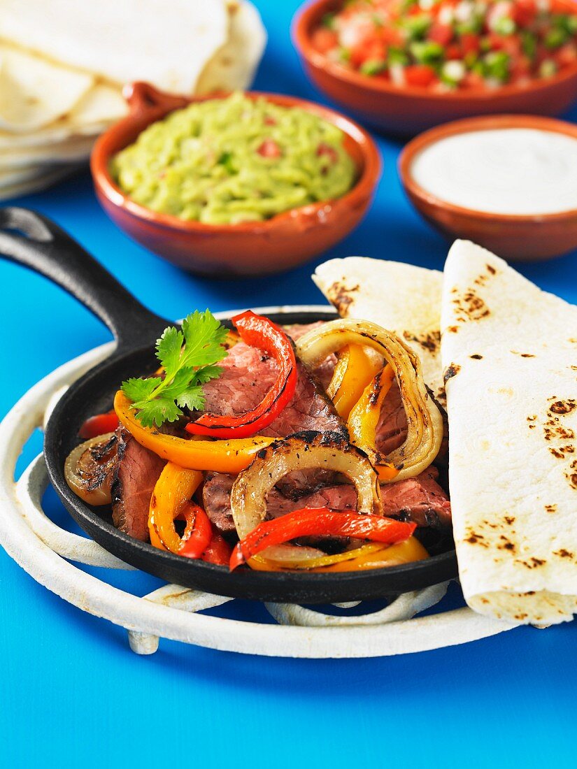 A pan of beef, onions and peppers with tortillas for fajitas