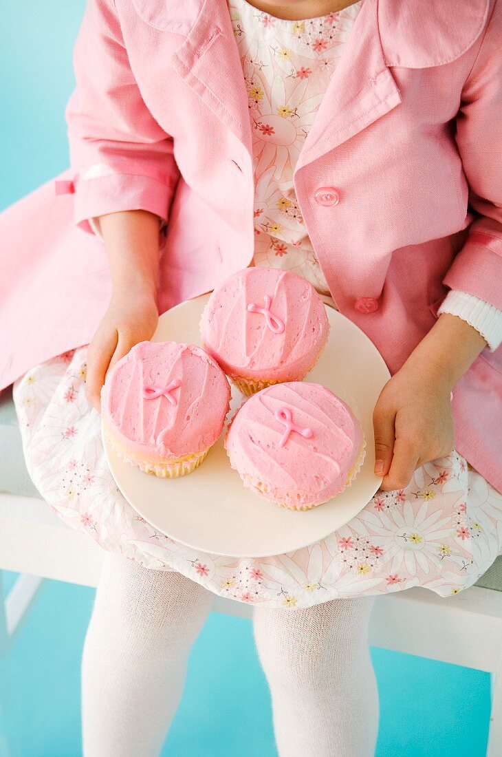 A girl dressed in pink holding a plate of pink cupcakes