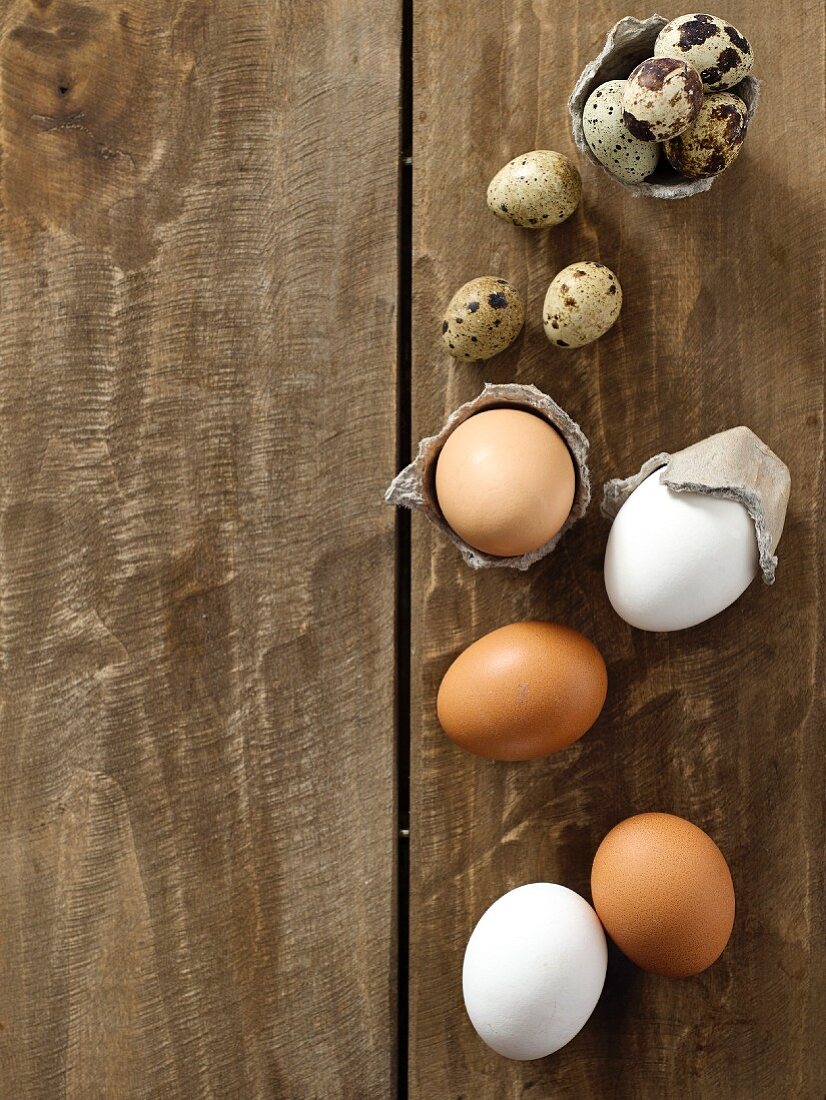 Brown and white chicken eggs and quail's eggs on a wooden surface