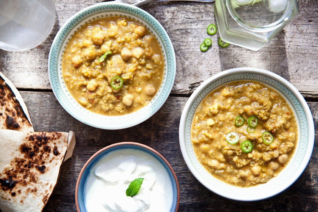 Two bowls of chana masala (chickpea curry) with unleavened bread and raita