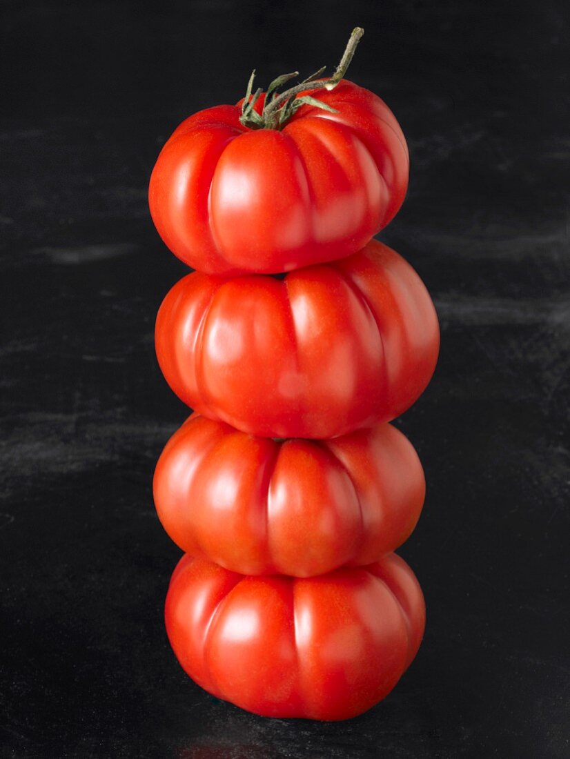 A stack of four beefsteak tomatoes against a black background