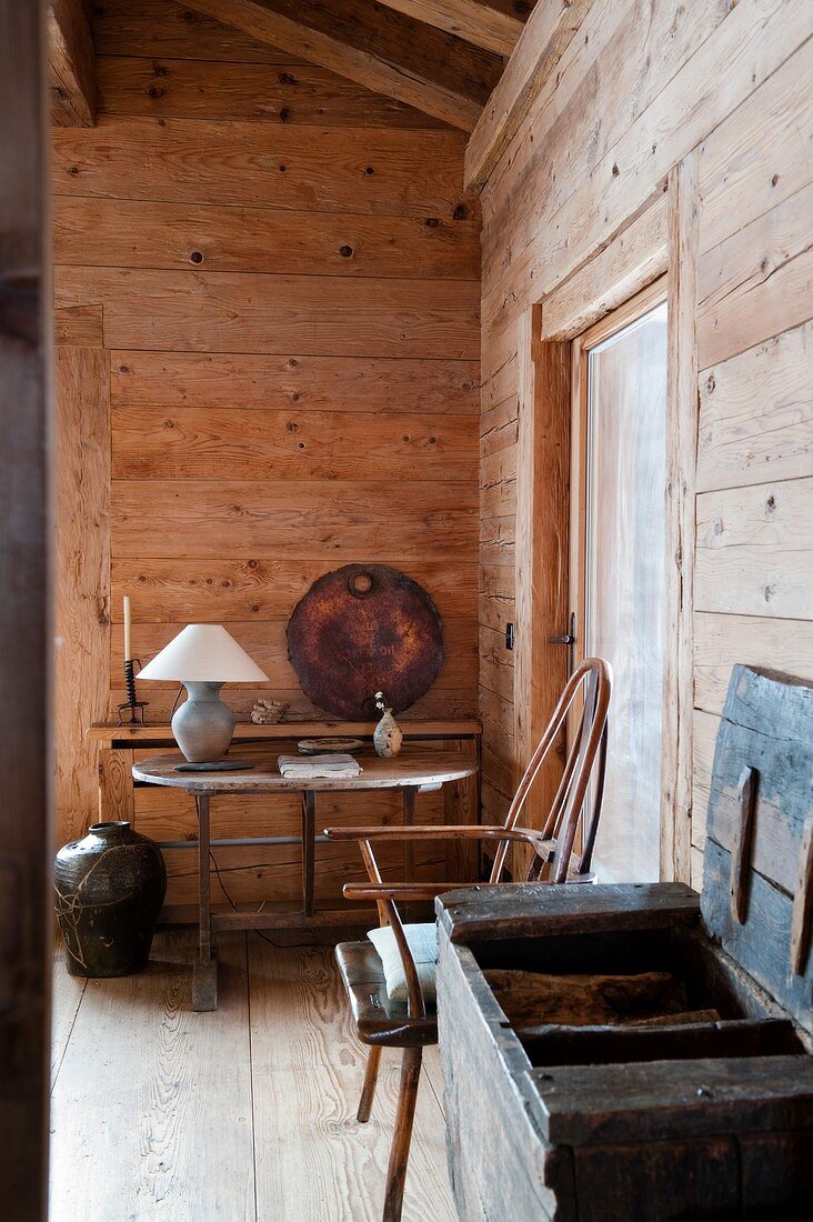 Open wooden trunk next to chair and table lamp on simple table in background in cabin living room