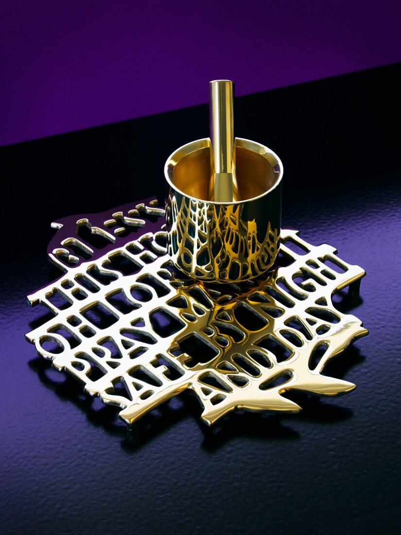 Brass mortar and pestle on trivet formed from connected lettering surrounded by violet surfaces