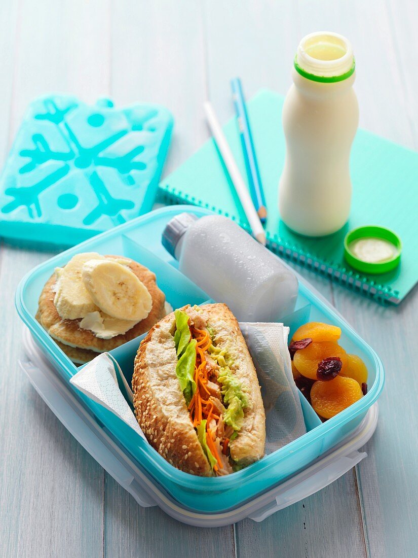 Lunchbox mit Thunfisch-Avocado-Sandwich, Trockenfrüchten und kleinen Pfannkuchen
