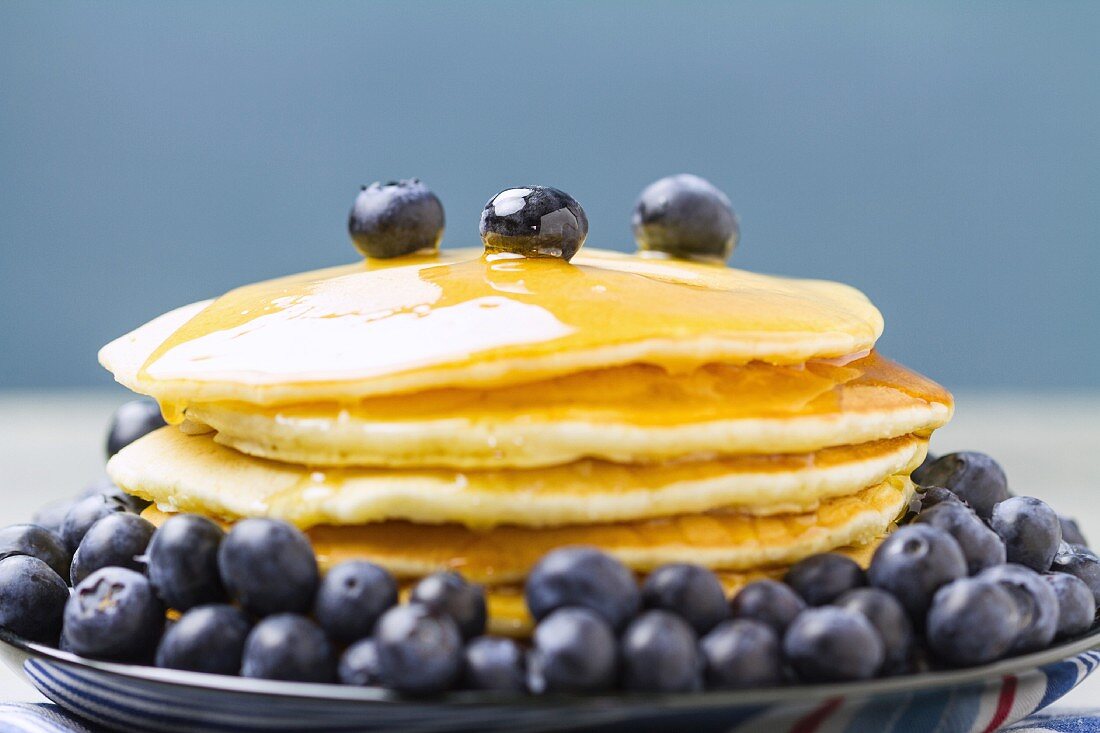 A stack of pancakes with maple syrup and fresh blueberries