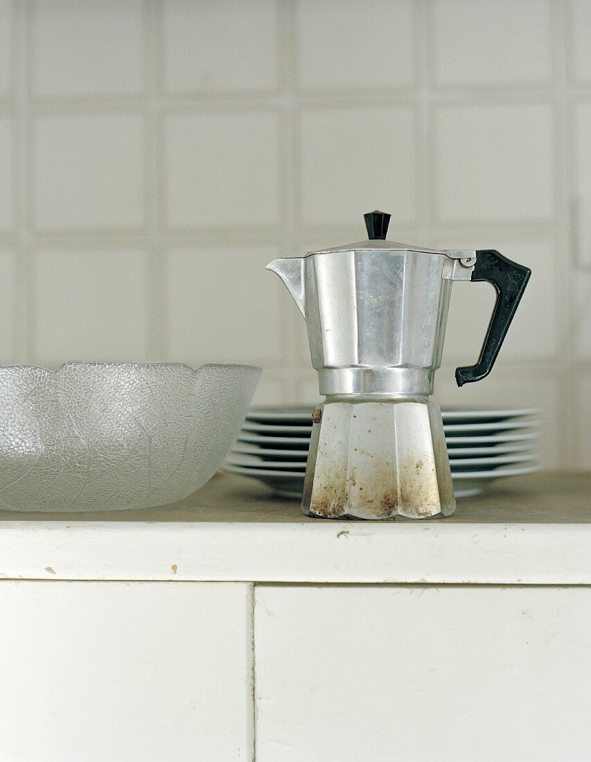 An espresso maker, a stack of plates and a glass bowl