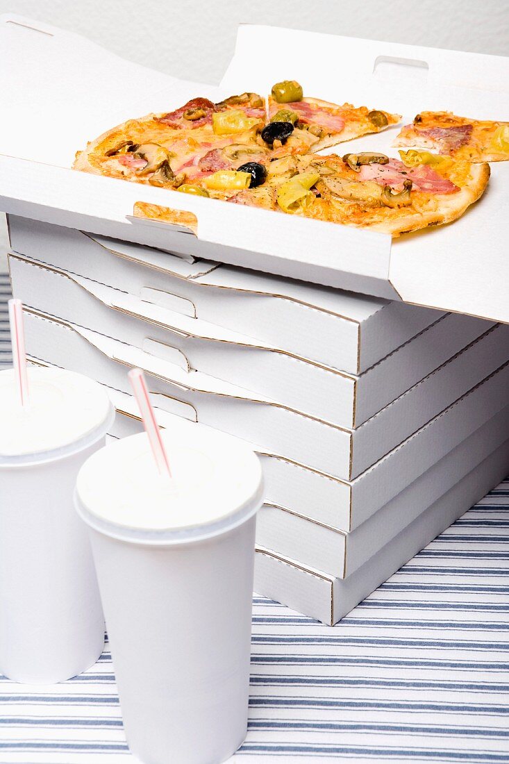 A stack of pizza boxes next to cups of soda