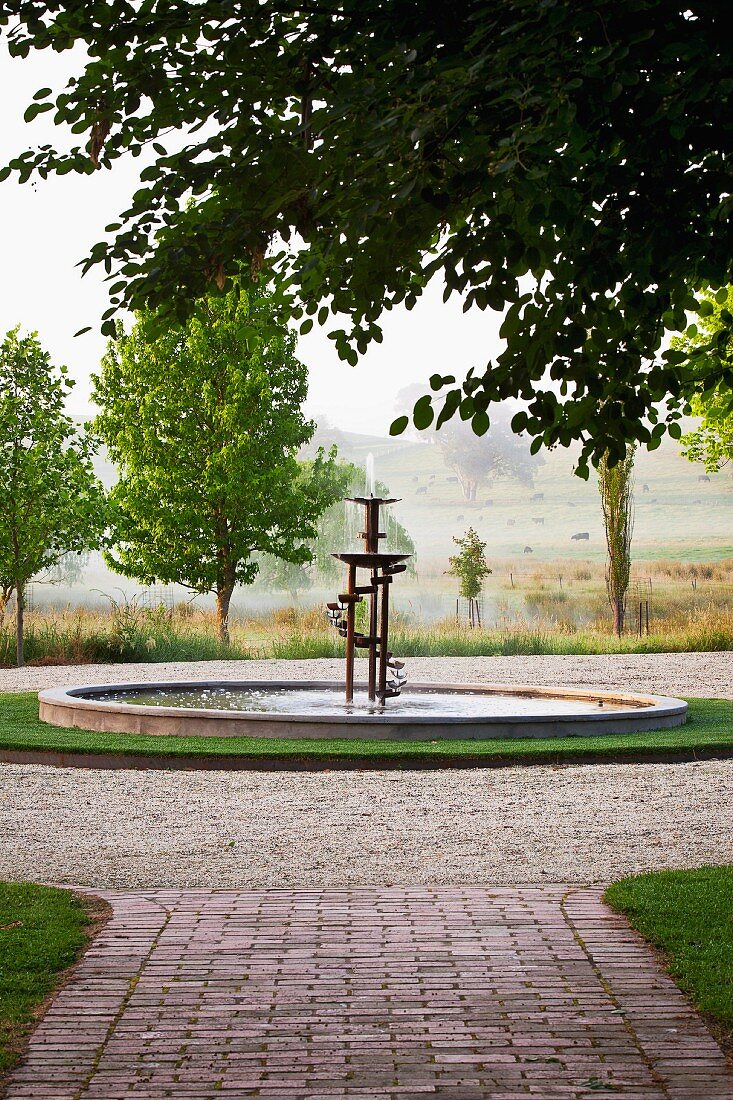 Atmospheric view of landscape with artistic fountain and paved garden path