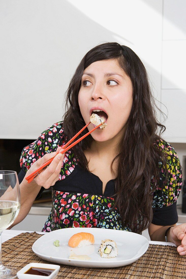 A young woman eating sushi in a kitchen