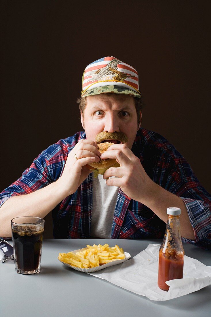 A stereotypical American man eating burger and fries with cola