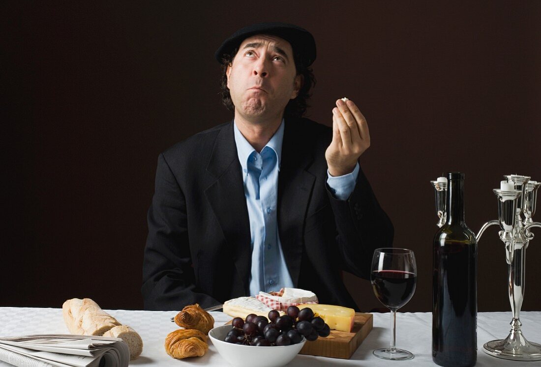 A stereotypical French man with a cheese platter, grapes and red wine