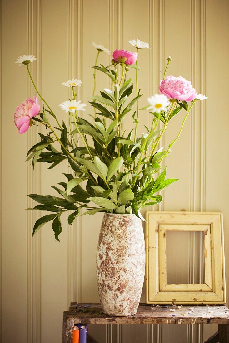 A vase of peonies and daisies and an empty picture frame