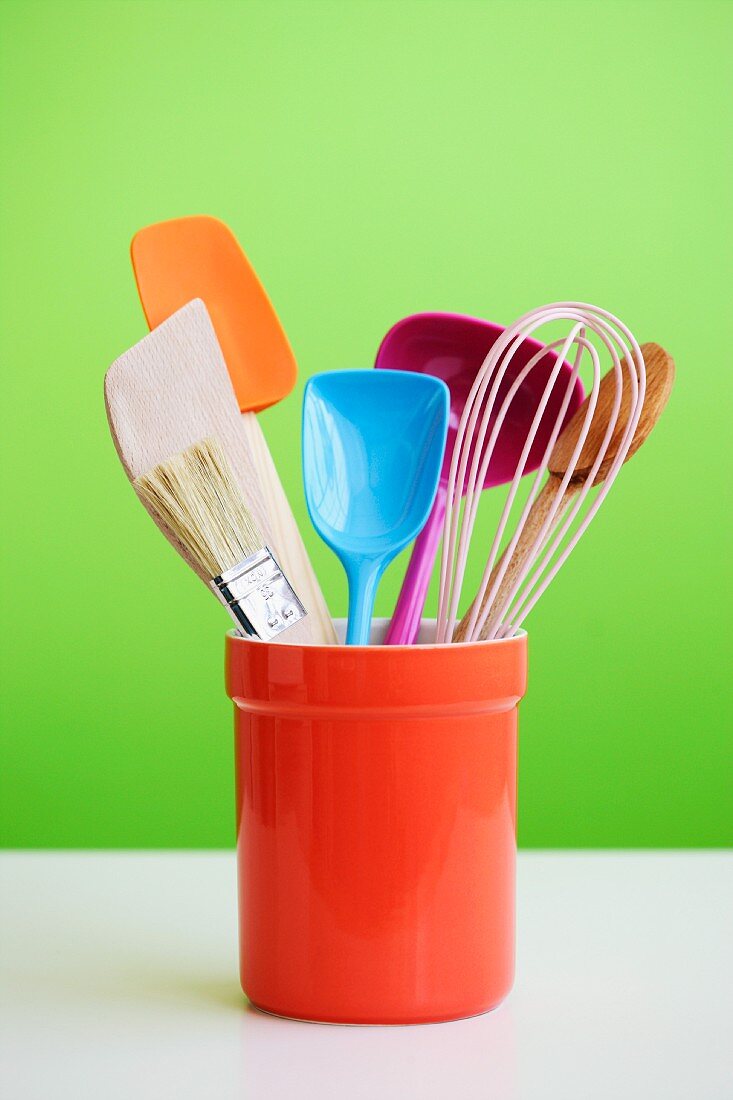 Colourful kitchen utensils in an orange ceramic pot