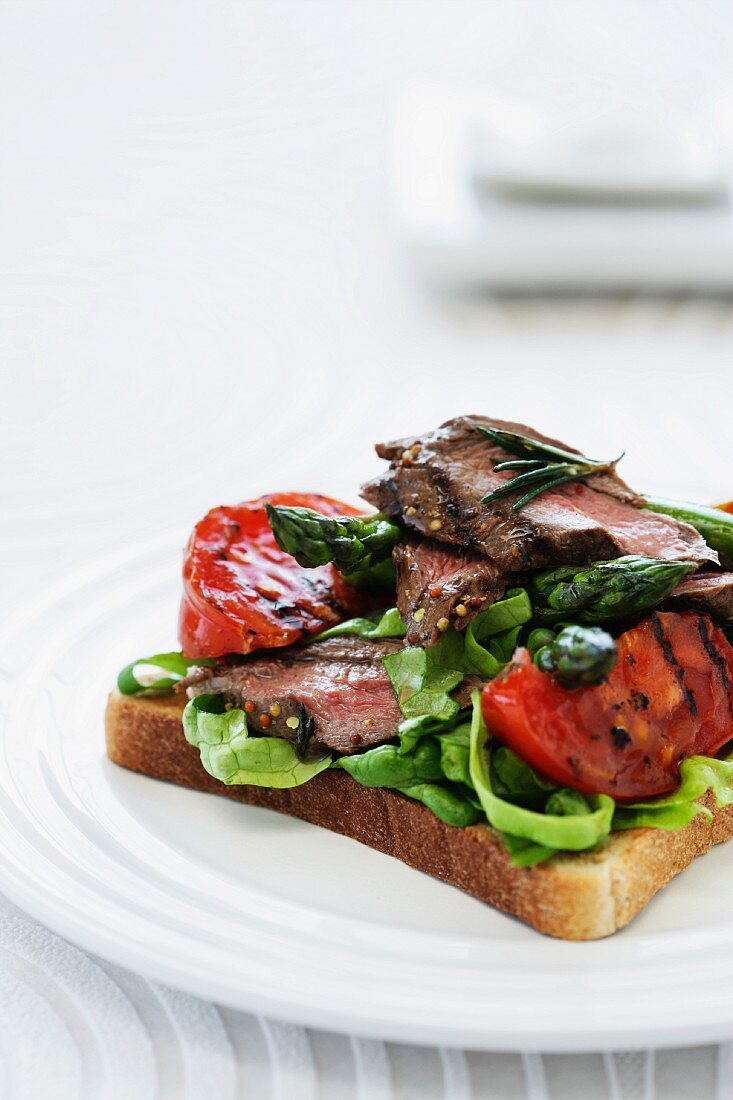 A slice of bread topped with grilled lamb, tomatoes and asparagus