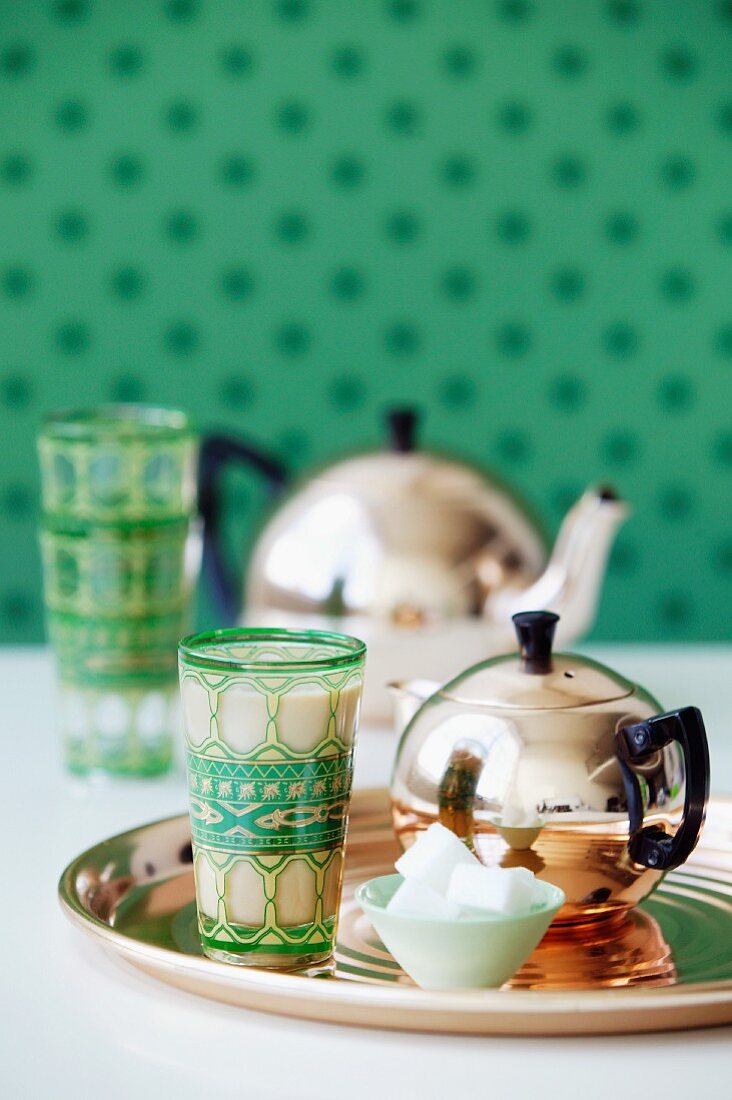 A glass of chai tea, a teapot and sugar cubes on a tray