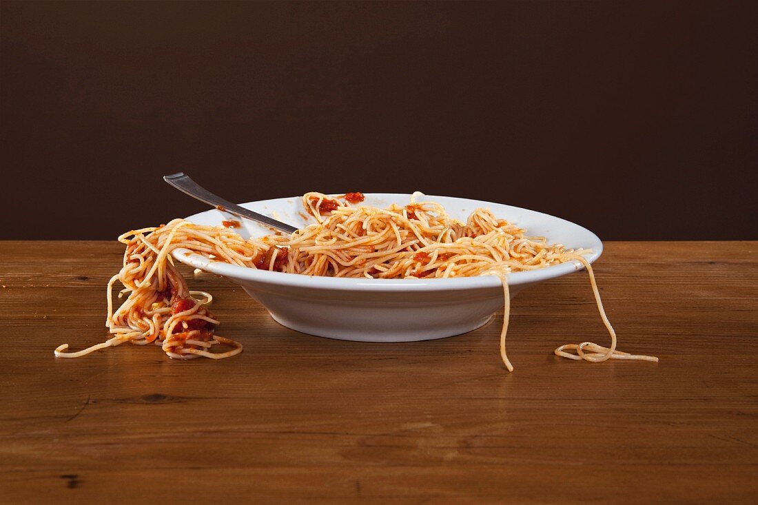 Spaghetti mit Tomatensauce, einige Nudeln hängen über Tellerrrand