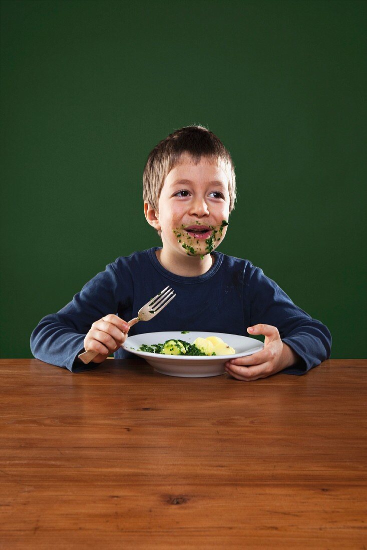 A boy smeared with spinach eating spinach with potatoes