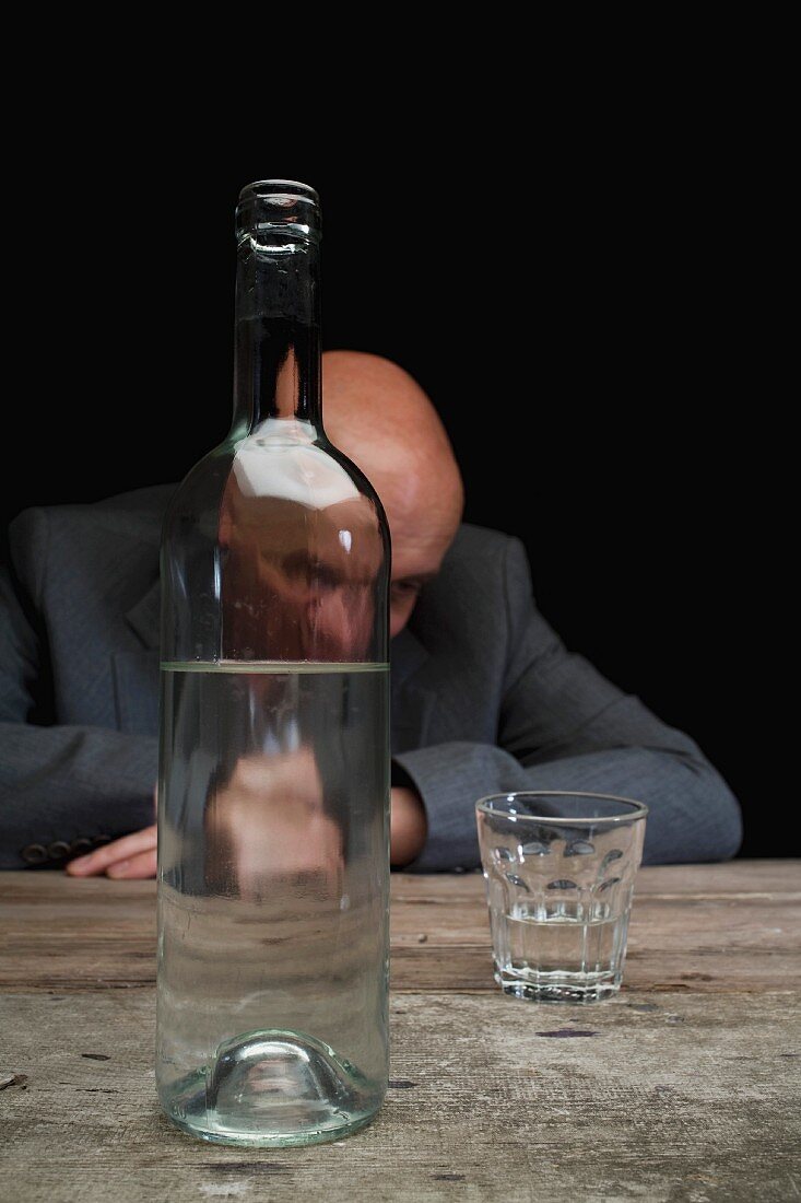 A depressed businessman with a bottle of schnapps and a half empty glass