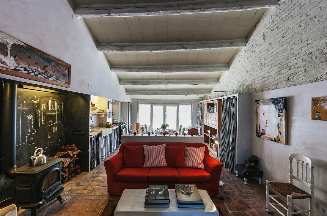 Offener Wohnraum mit rotem Sofa und Holzofen, Wandnische mit Kreidewand, im Hintergrund Küchen mit Essbereich