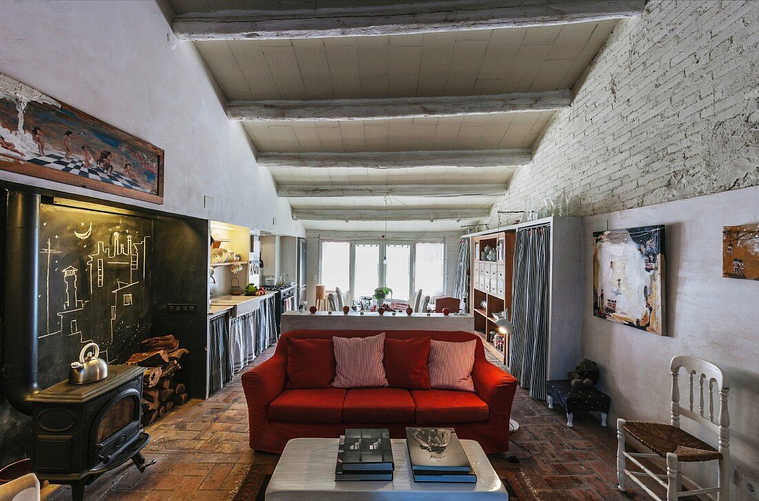 Open-plan interior with red sofa, wood-burning stove, blackboard in niche and kitchen-dining area in background