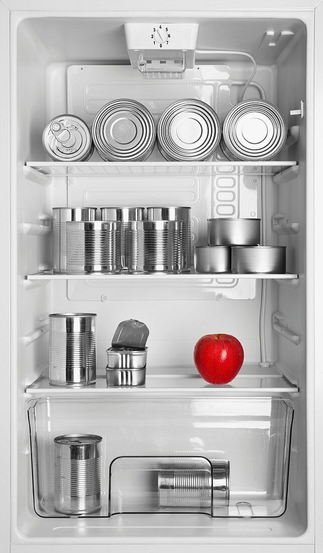 Various tins and a red apple in an open fridge