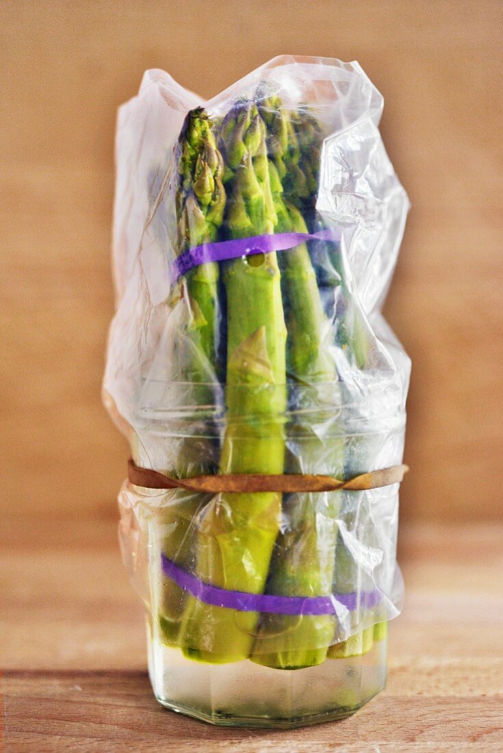 Spargel frischhalten: Grüne Spargelstangen mit Frischhaltebeutel in Glas mit wenig Wasser stellen