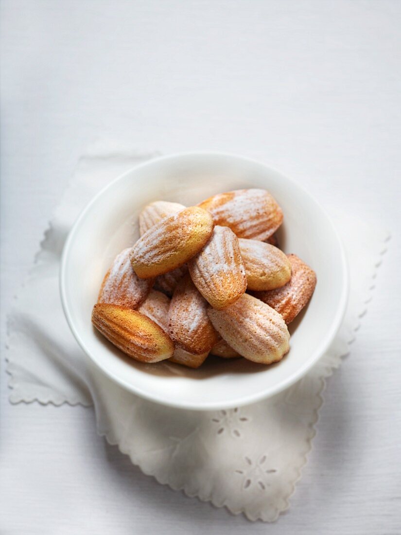 A bowl of madeleines with icing sugar