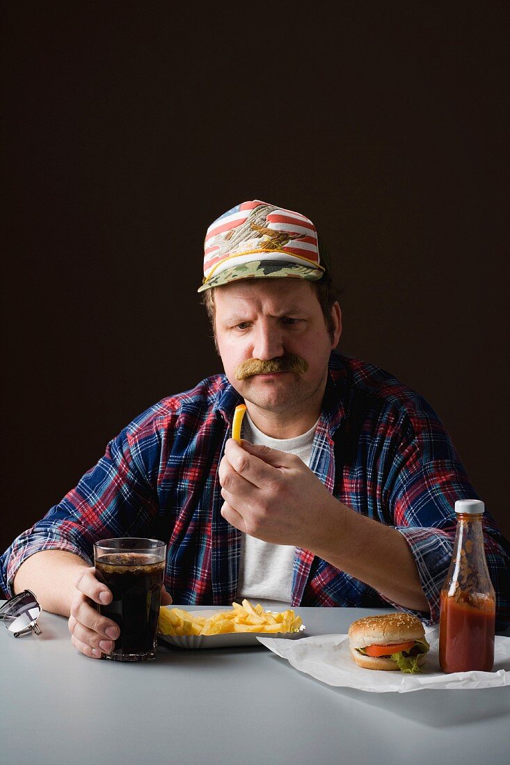 Typisch amerikanischer Mann schaut auf Pommes frites in seiner Hand