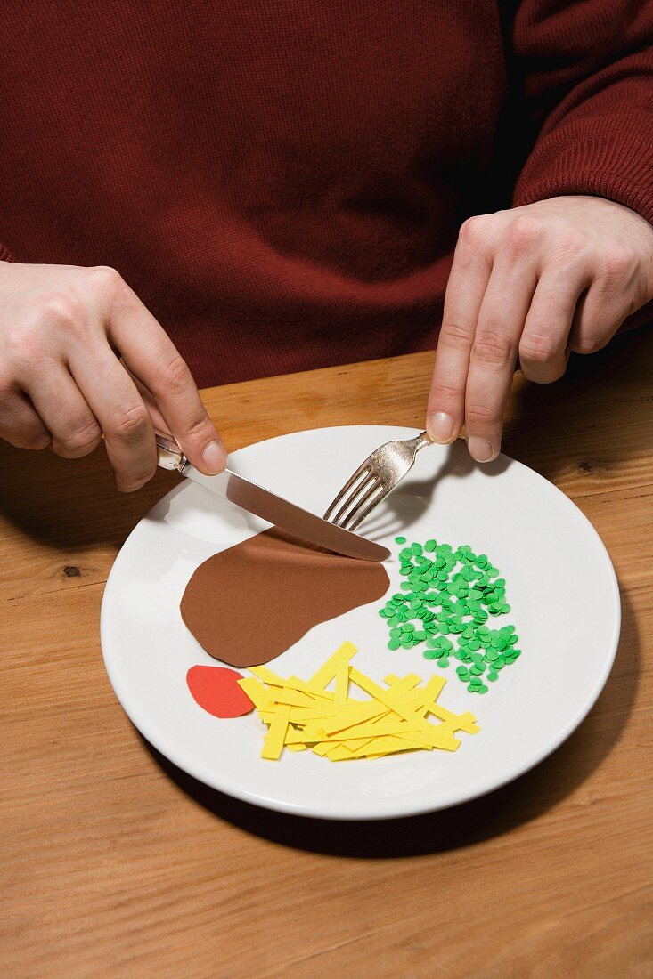 A man with a plate of steak, chips, peas and ketchup made from paper
