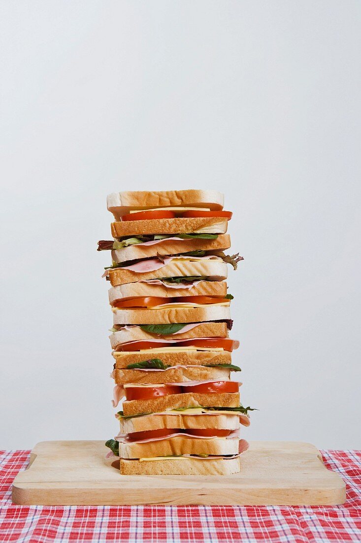 A stack of ham, cheese and tomato sandwiches on a chopping board