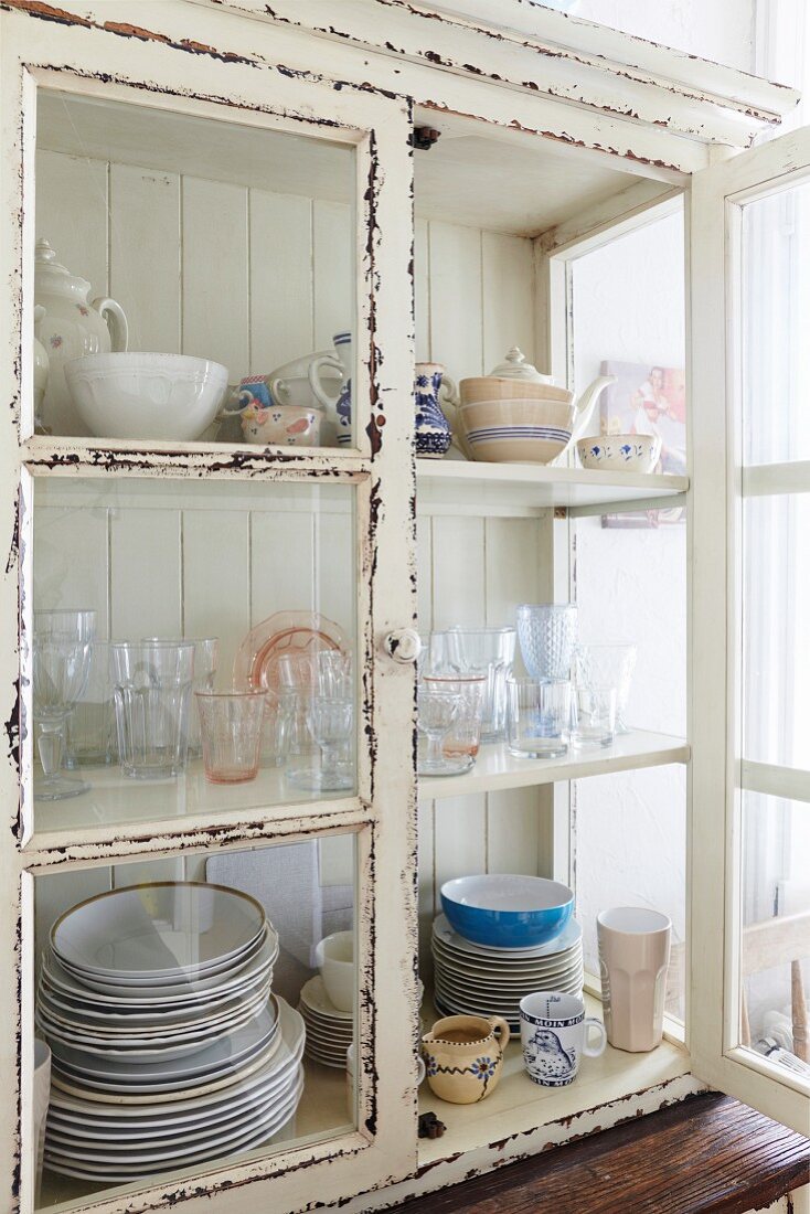 Crockery in glass-fronted cabinet with peeling white paint