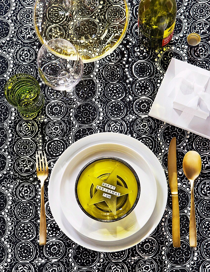 Festive table setting with green glass star in bowl and gilt cutlery on black and white printed tablecloth