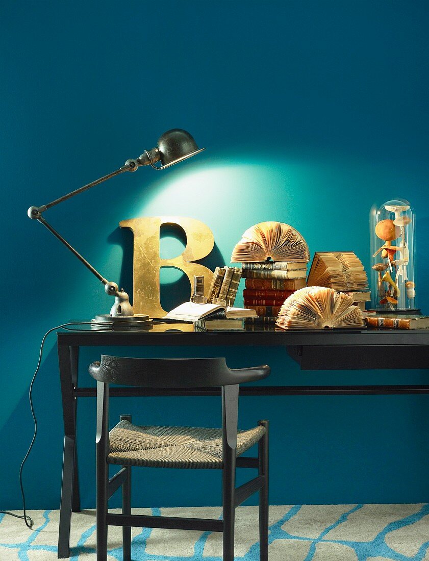 Jointed table lamp, decorative letter and antiquarian books on desk against blue wall
