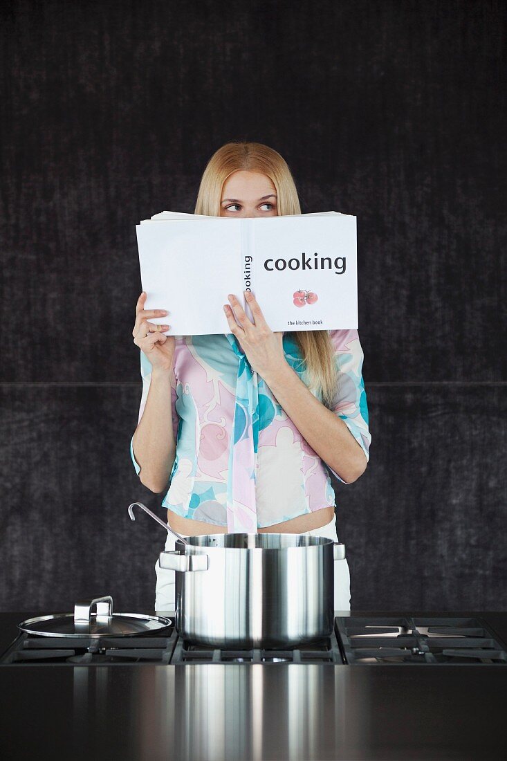Frau mit Kochbuch vor dem Küchenherd