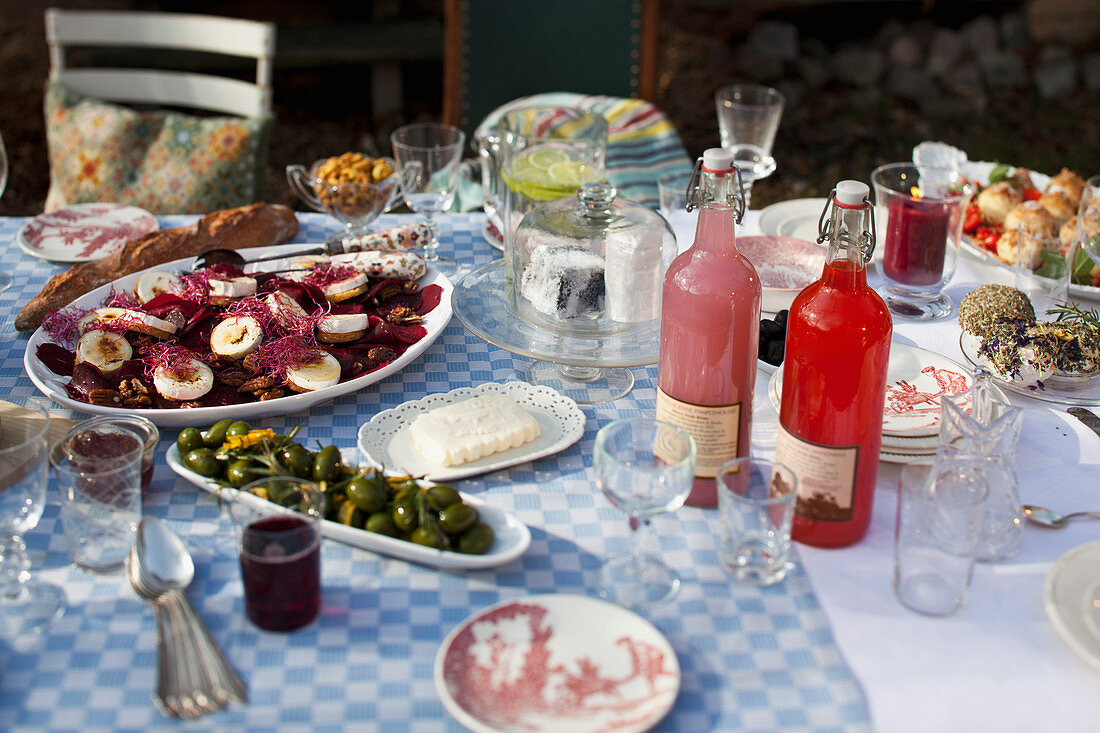 Gedeckter Tisch im Garten mit Ziegenkäse, eingelegten Birnen, Oliven, Brot und Getränken