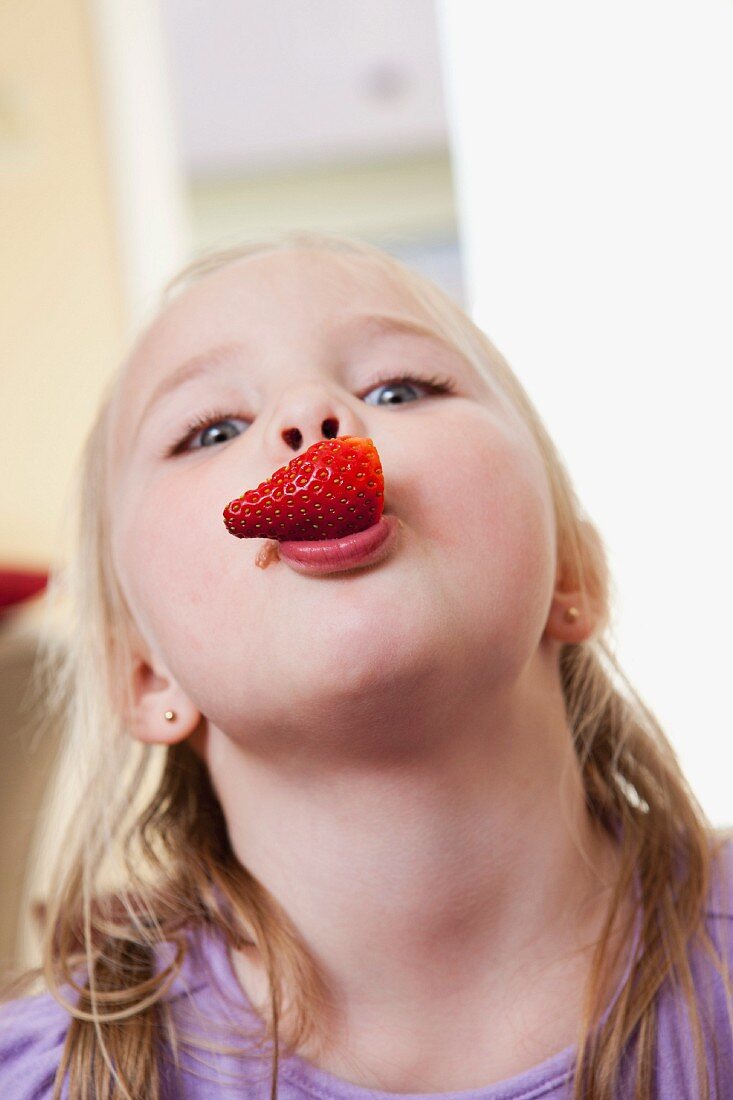 A blonde girl with a strawberry in her mouth