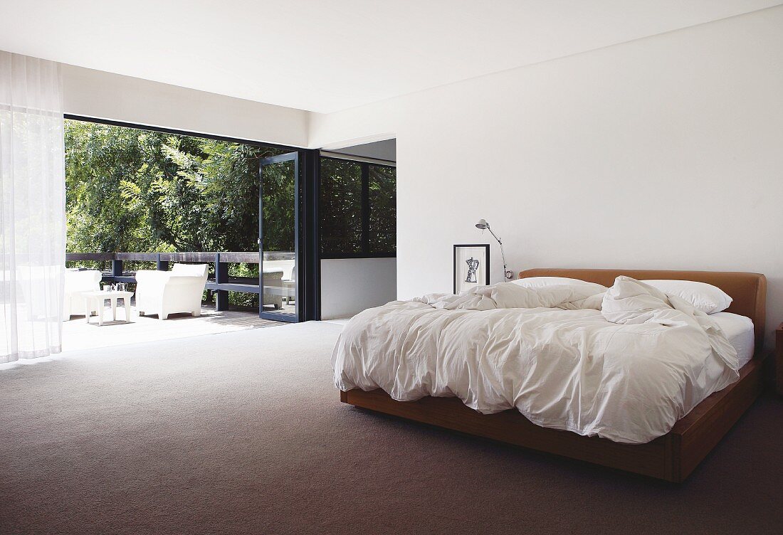 Minimalist bedroom with double bed and open folding terrace door with view of garden