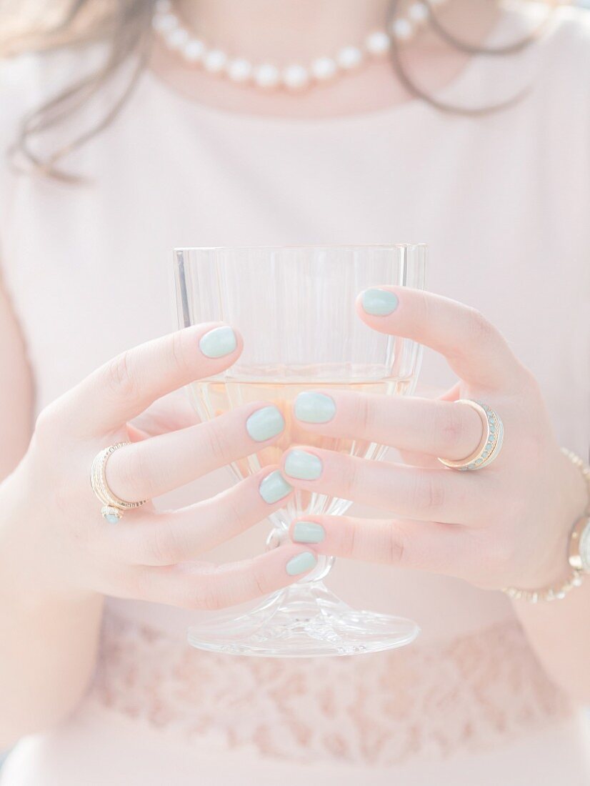 An elegantly dressed young woman holding a glass of white wine