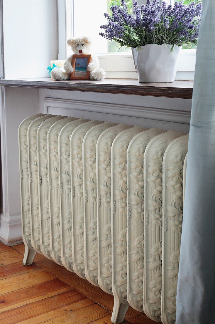 Antique radiator on legs below window and potted, purple-flowering on windowsill