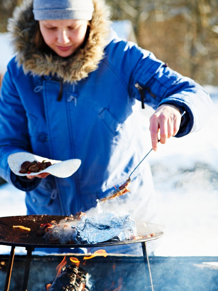 A woman grilling sausages at a winter picnic