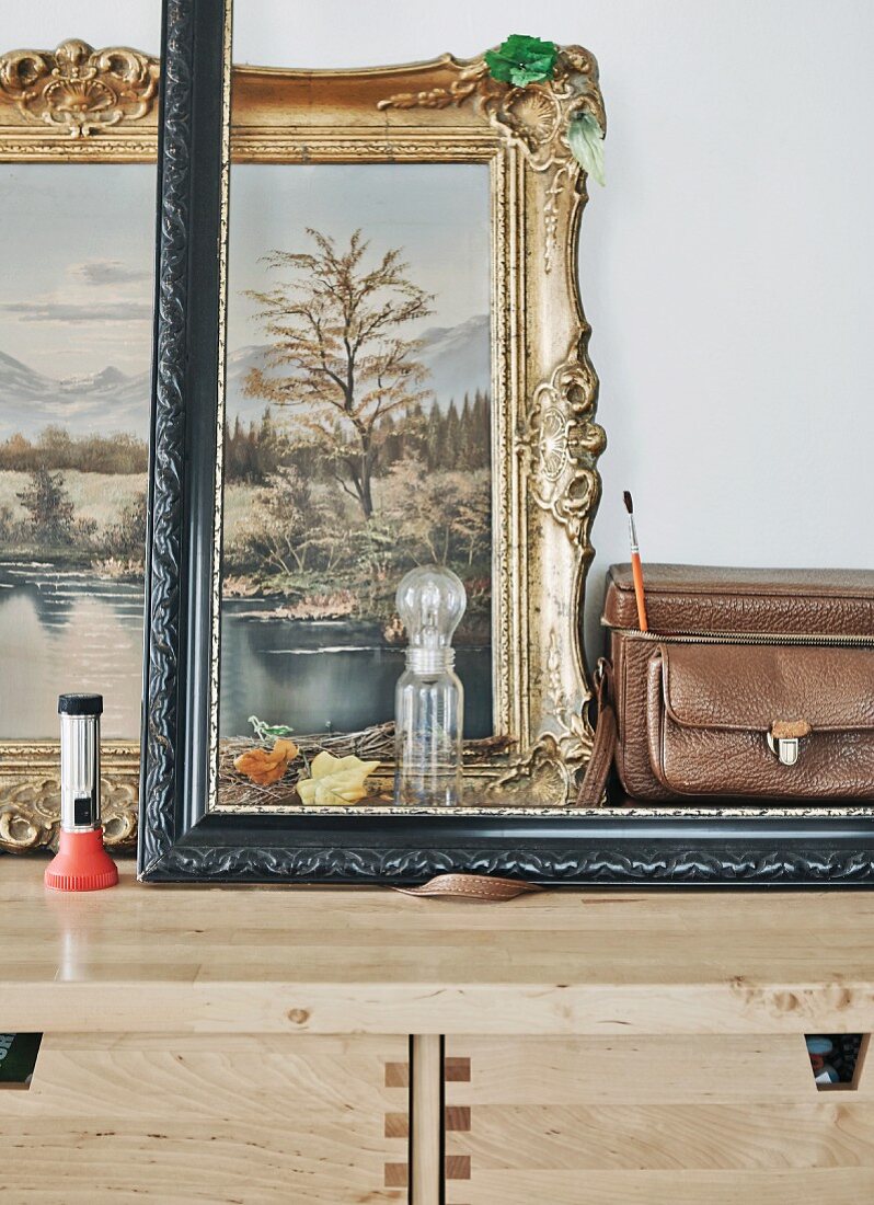 Empty picture frame, vintage objects and gilt-framed oil painting on stripped wood chest of drawers
