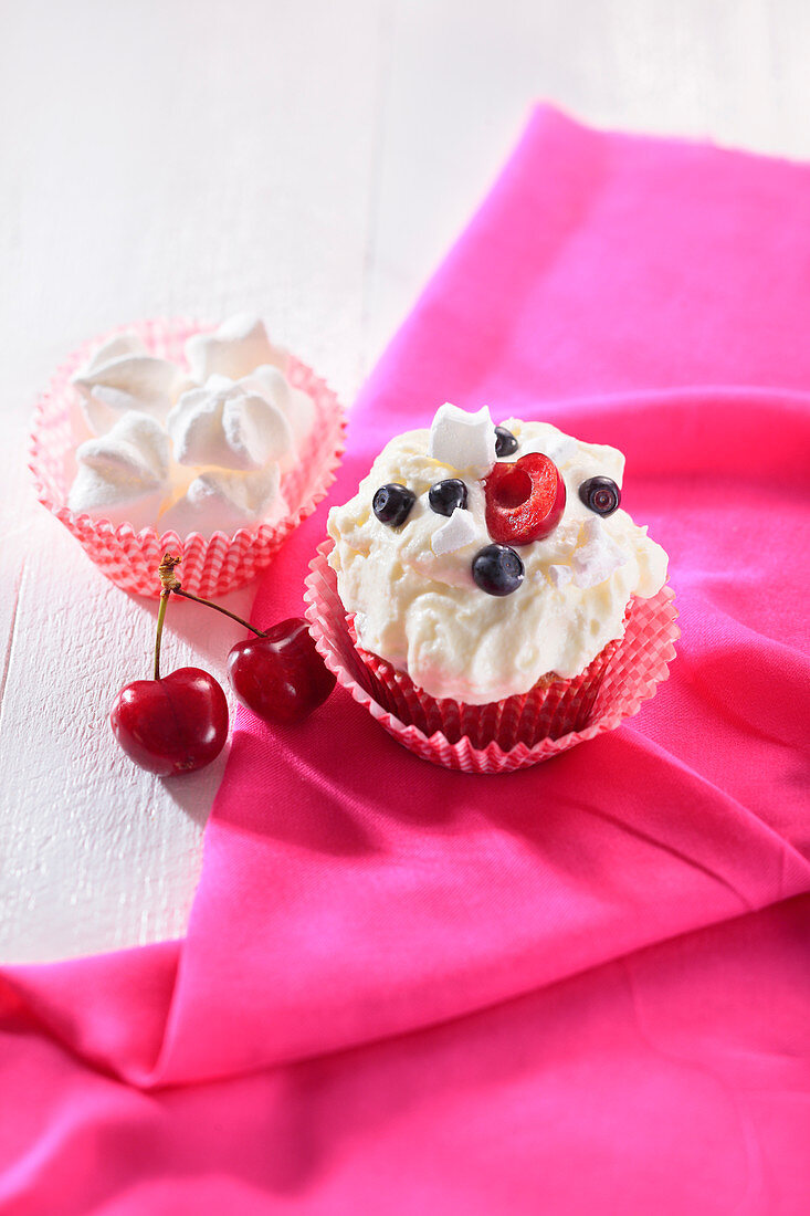 A cupcake topped with meringue, blueberries and cherries