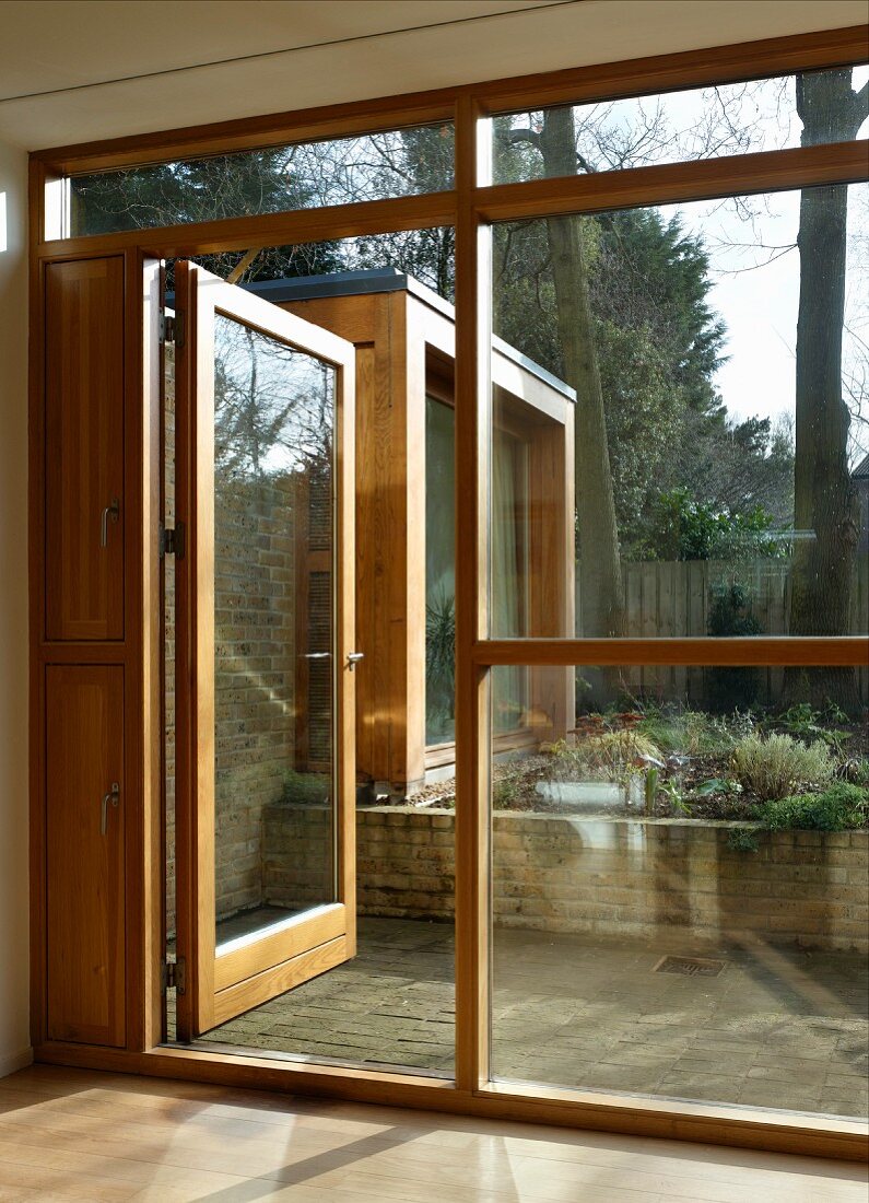 Bank of windows with wood-glass construction and open patio door with a view of a flower bed