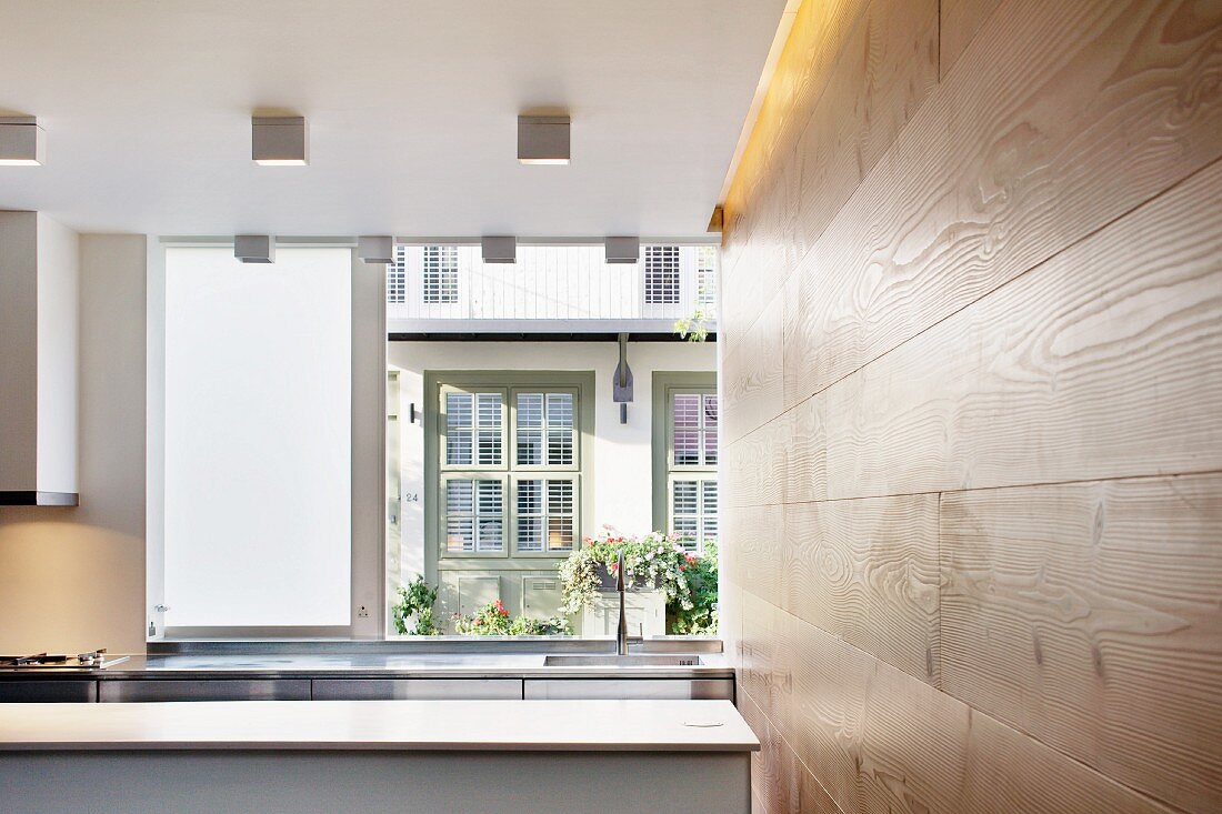 Open kitchen next to a wood panel wall and a view through a window of the neighboring house
