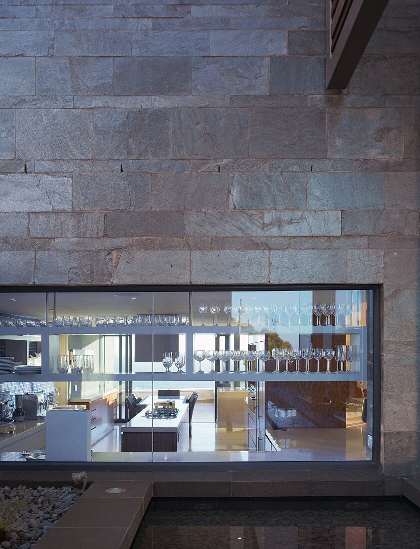 Modern new building with a facade of natural stone and a bank of windows in the first floor with built-in shelves and drinking glasses