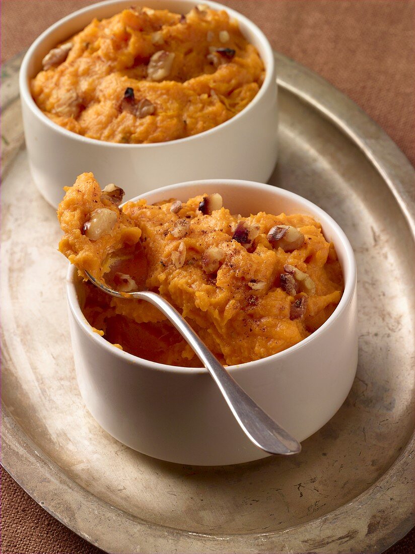 Two Bowls of Mashed Sweet Potato with Walnuts on a Metal Tray; One with Spoon