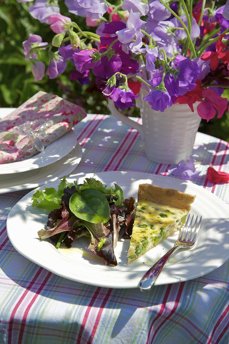 A slice of pea and bean quiche with a mixed leaf salad